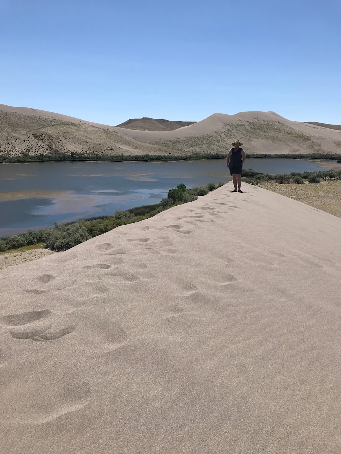 Girl on top of a sand dune with a lake and more sand dunes in the background during an Idaho State Parks Challenge