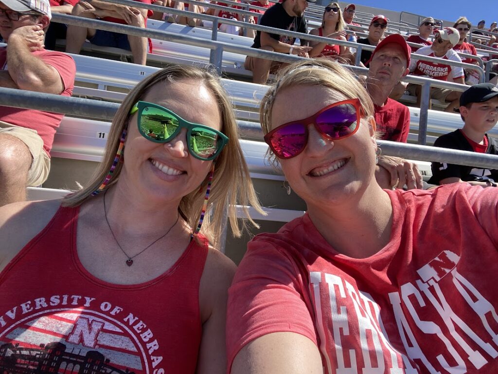 Two girls in red shirts at a Nebraska Huskers football game.
