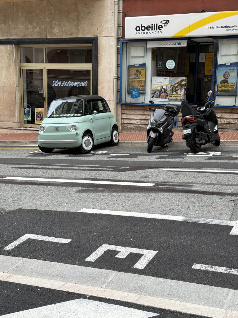 Small mint green Fiat parked next to scooters.